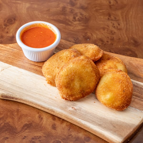 Golden-brown fried ravioli and a small white cup of red marinara sauce on a wooden board.