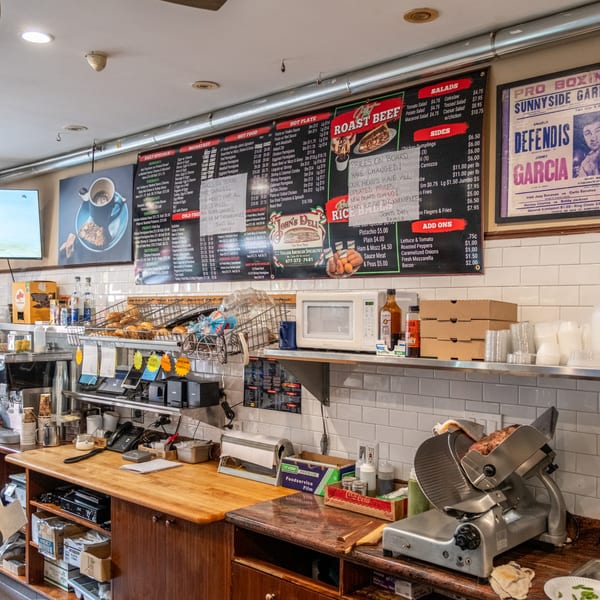 A deli counter at John's Deli with menus, food displays, and a meat slicer.