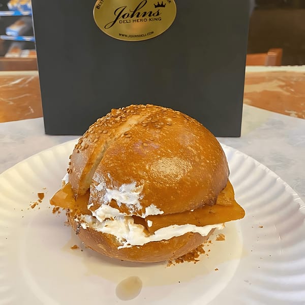 A John's Deli bagel with cream cheese and lox on a white paper plate.