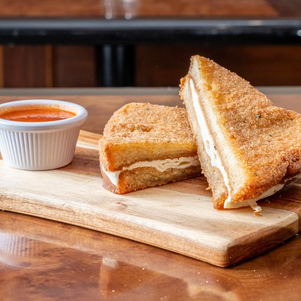 Two halves of a breaded sandwich with creamy filling and a side of tomato soup on a wooden board.