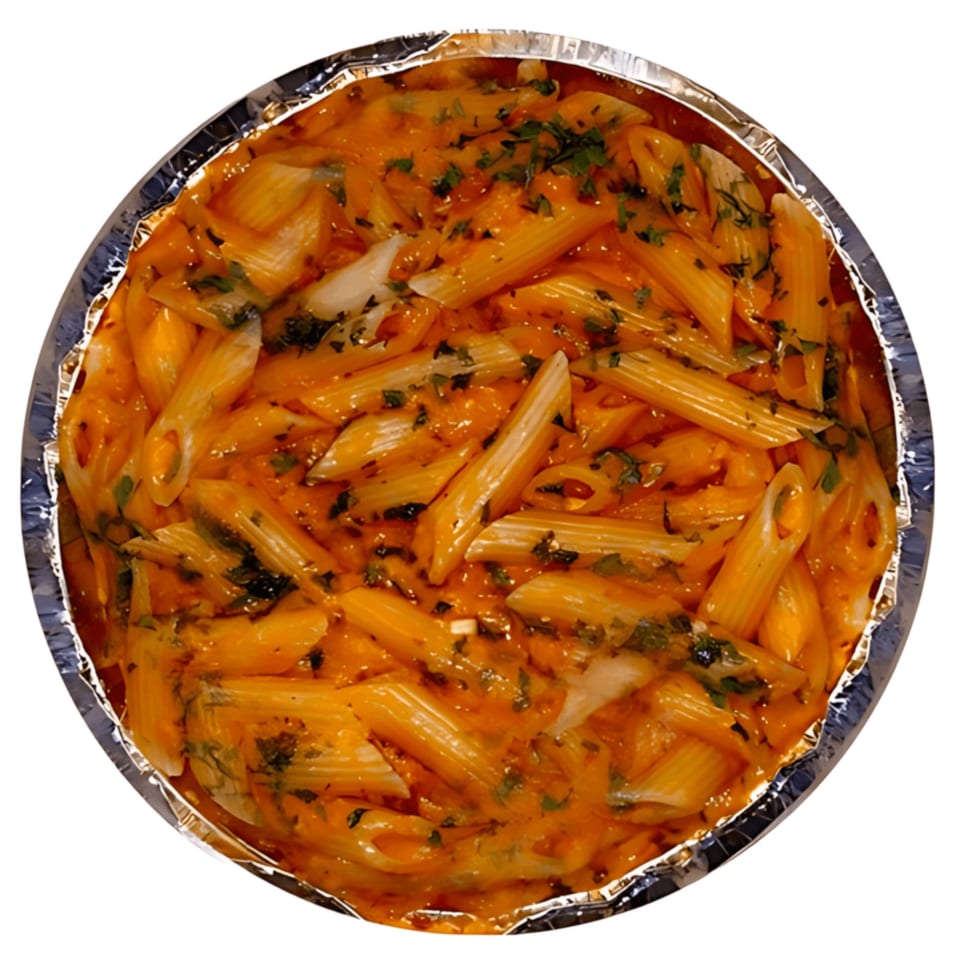 Penne pasta in a creamy orange sauce with green herbs, served in a foil container.