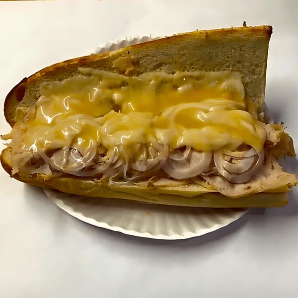 John's Deli turkey and cheese sub sandwich with melted cheese and onions on a paper plate.